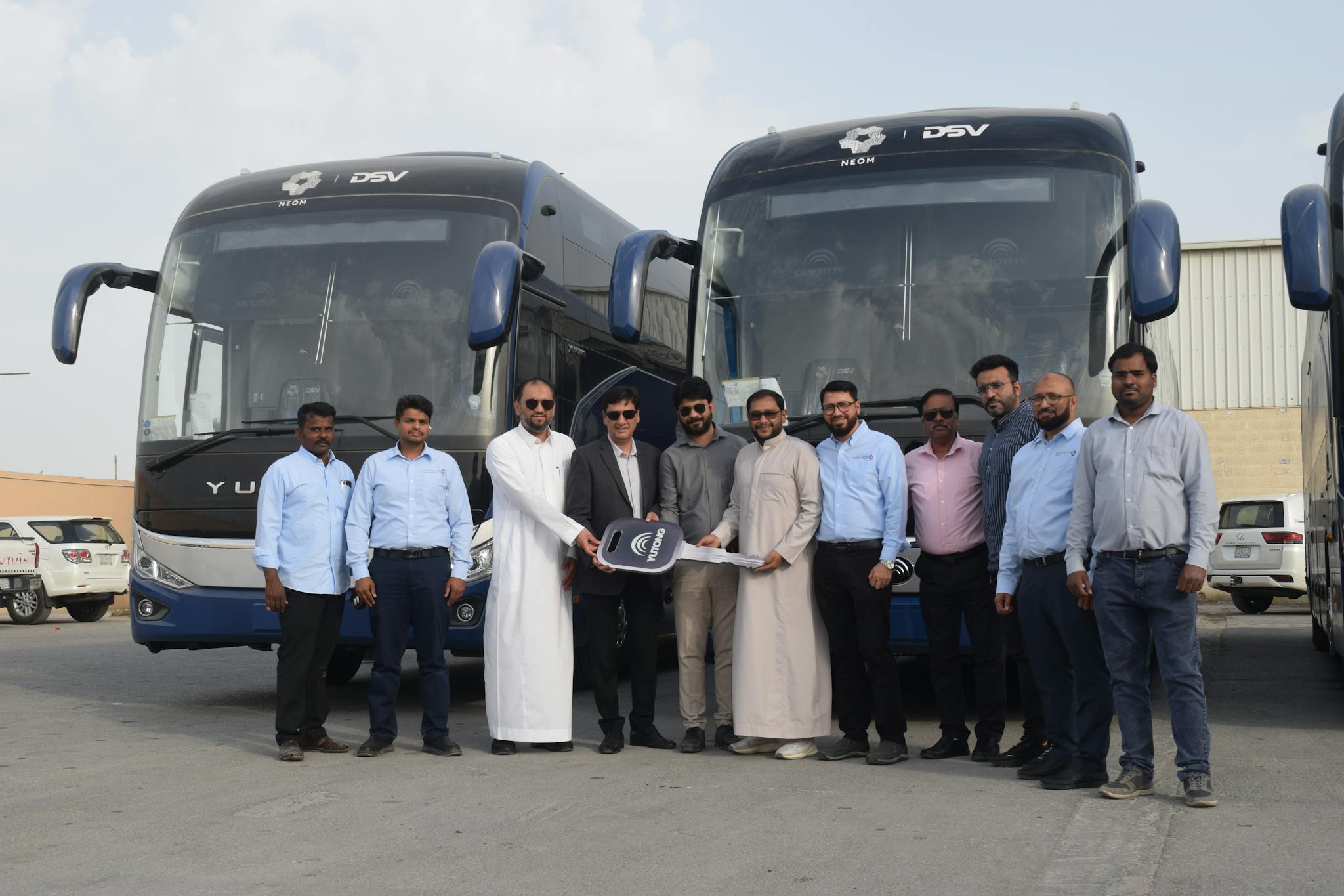 Group of businessmen standing in front of parked buses holding a large key.